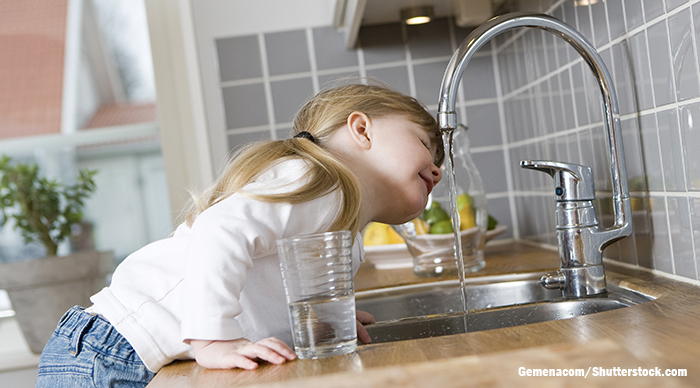 child drinking water from faucet at kitchen sink